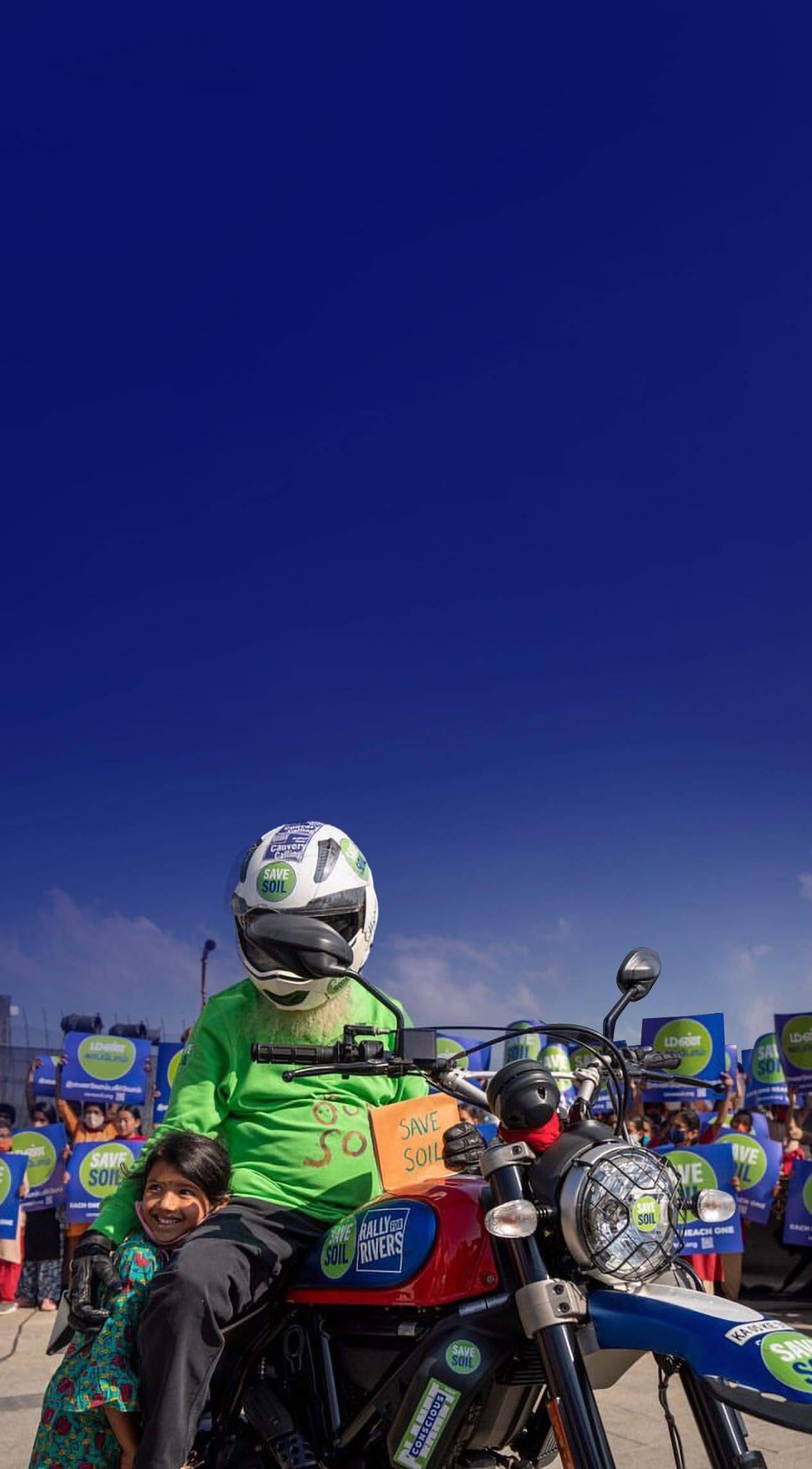 Sadhguru na motorju, poleg deklice, obdan z napisi Save Soil (Rešimo prst)
